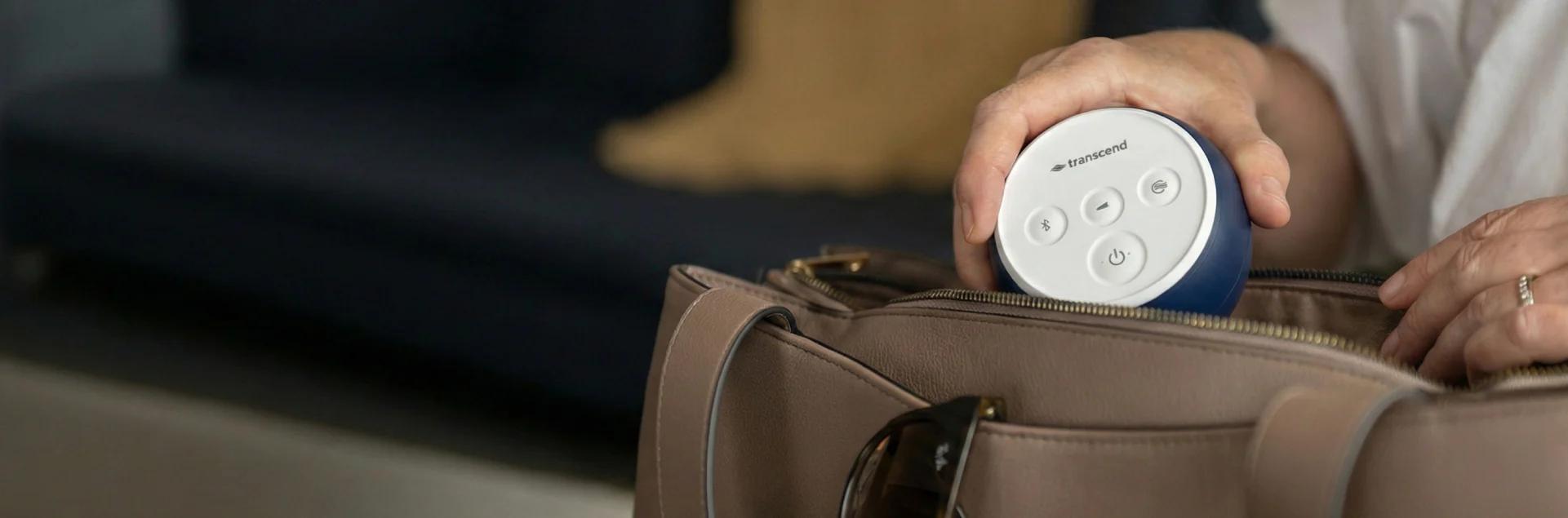 A hand tucking the navy Transcend Micro 510 travel CPAP into the top of a leather weekender bag