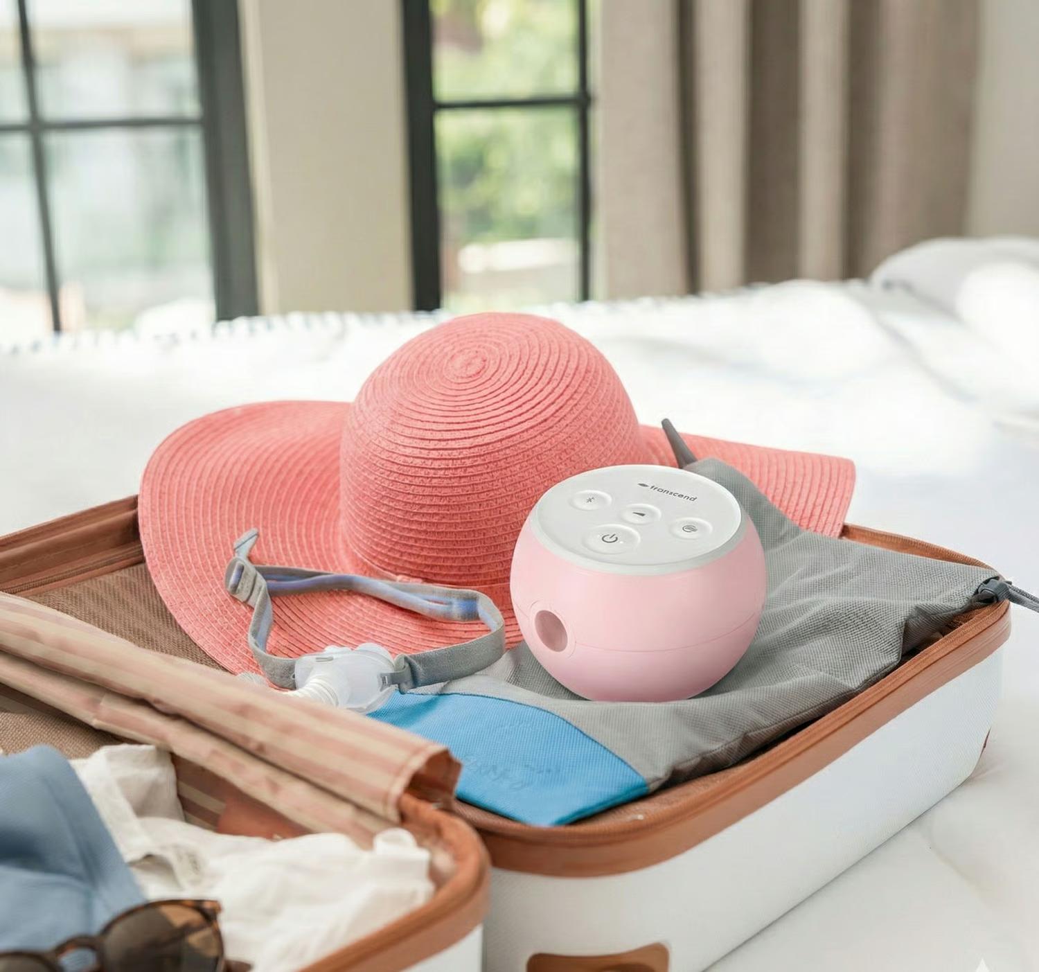 A Petal Pink Transcend Micro 510 packed in an open suitcase with a sun hat and CPAP mask