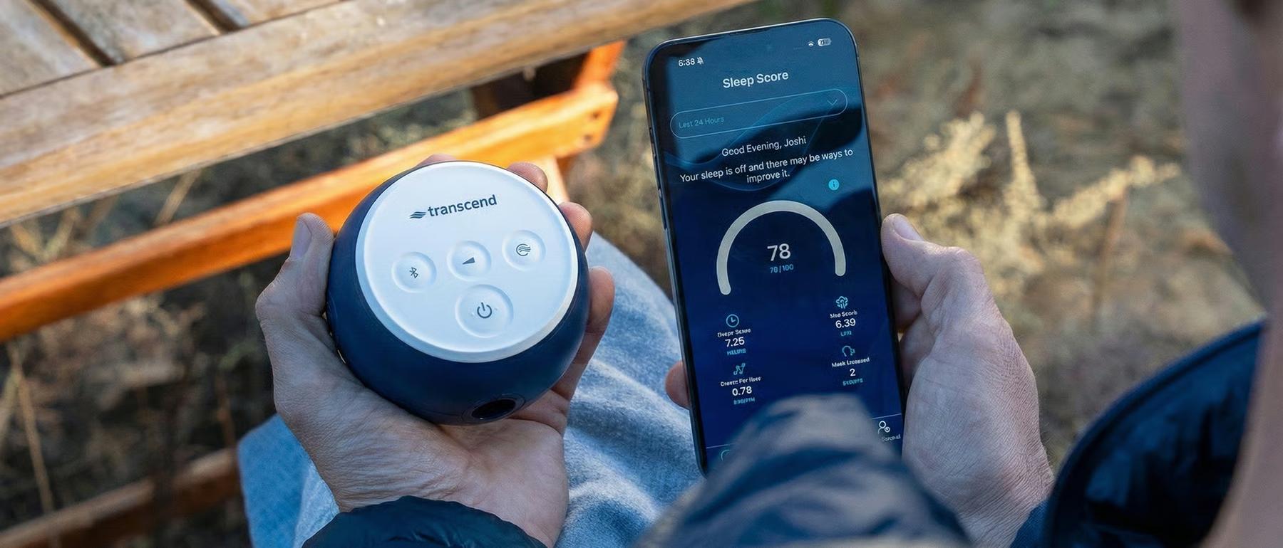 A person holds a round Transcend Micro travel CPAP and a smartphone showing a sleep score tracking app.